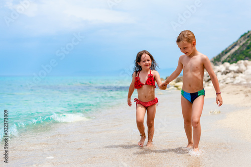 Siblings are smiling and walking on the beach © Jovan
