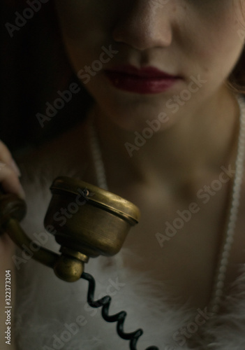 Close up view of young female model face lower part. Girl with red lips vintage make up portrait. Girl holding vintage telephone handset carefully.