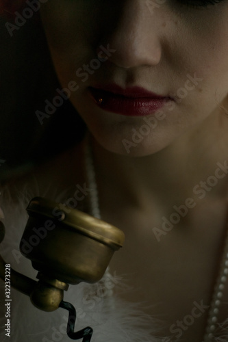 Close up portrait selective focus view of  young adult female dressed in 1920s fashion style talking on old vintage telephone. Red lips make up extreme close up view.