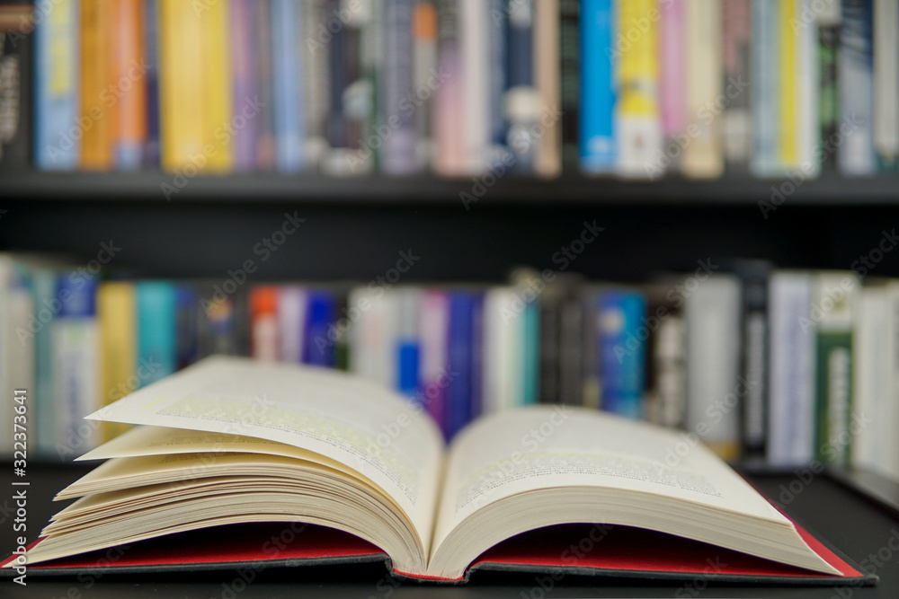 An open book on a working table and a bookshelf in background An open book on a working table and a bookshelf in background