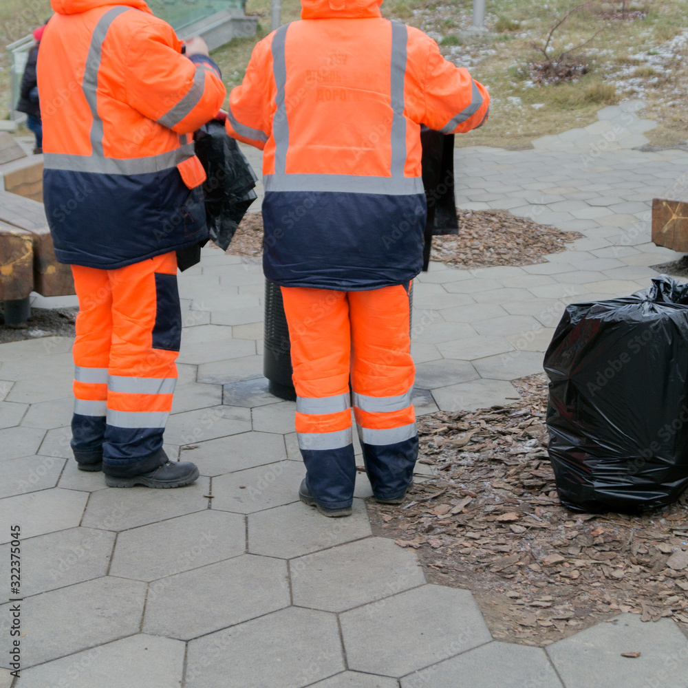 Workers in overalls clean up trash on the street.