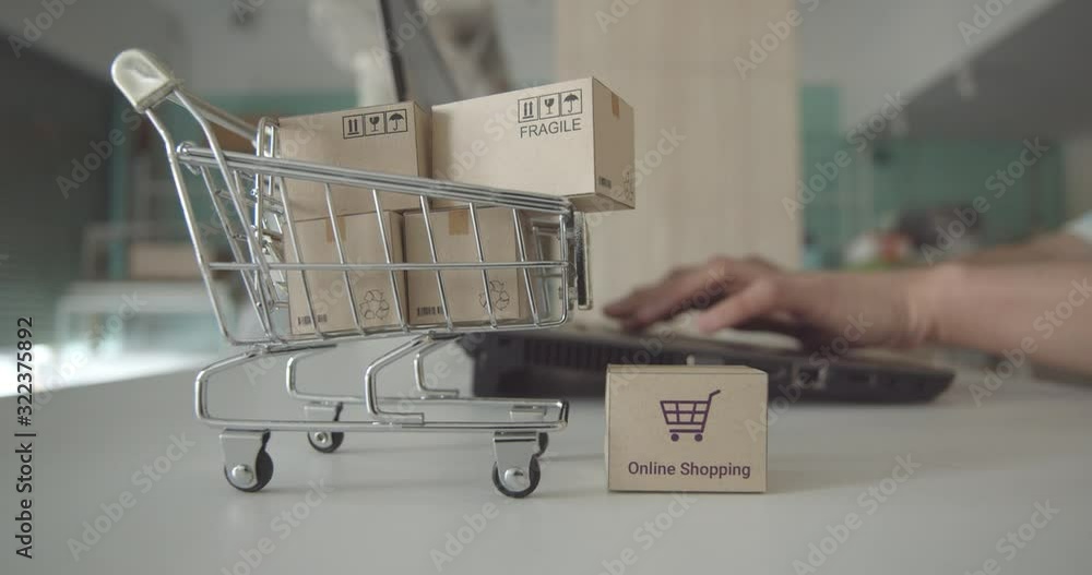 Online shopping / ecommerce and delivery service concept : Paper cartons with a shopping cart or trolley logo, user uses a laptop, depicts customers order things from retailer sites via the internet.