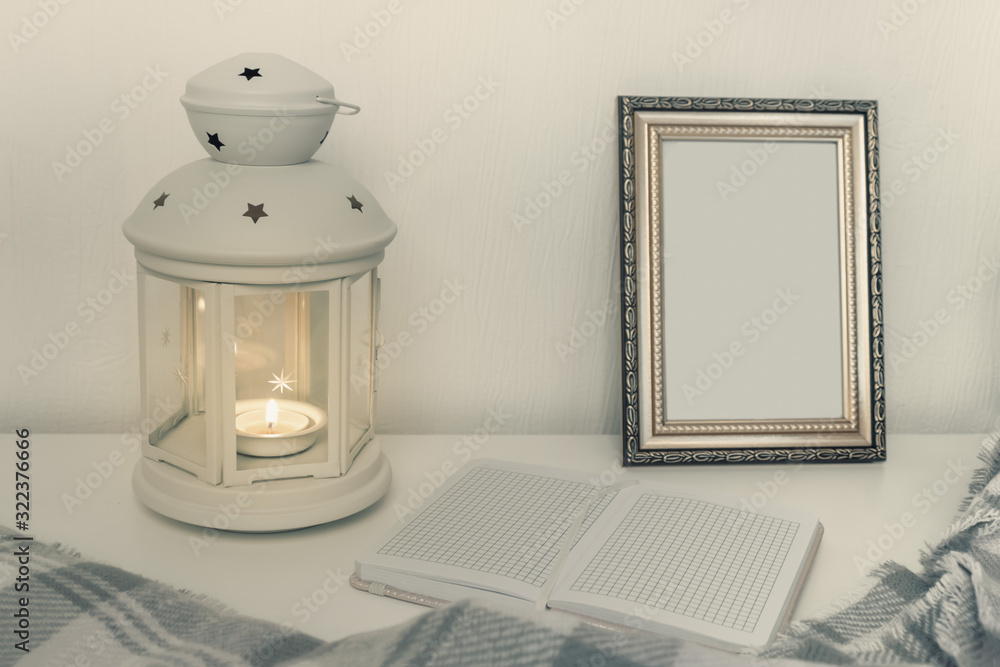 Winter still life interior details, lantern with burning candle, open book and a photo frame on the table Winter still life interior details, lantern with burning candle, open book and a photo frame on the table