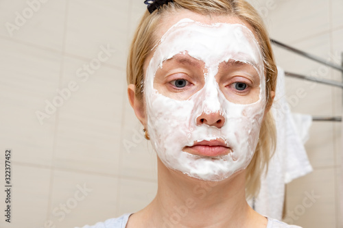 A portrait of a sad woman with problem acne skin making a cleansing purifying white facial mask, anti black spot and acne treatment, copy space