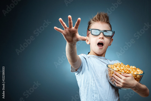 A boy holding popcorn in his hands watching a movie in 3D glasses, fear, blue...