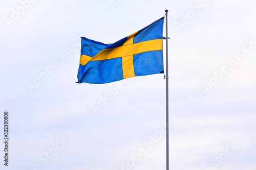 Sweden national flag on flagpole waving in the wind. Blue-yellow flag of Sweden on blue sky background, selective focus. Stockholm state symbol. 