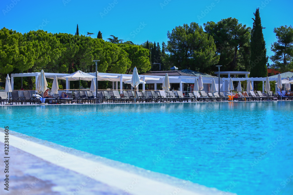 Swimming pool on outdoor zone of hotel.Umbrellas and sun protection tents for quests.Sunshine clear blue water with sunny reflections.Summer holidays and vacation.Tourism in Europe, Slovenia,Portoroz