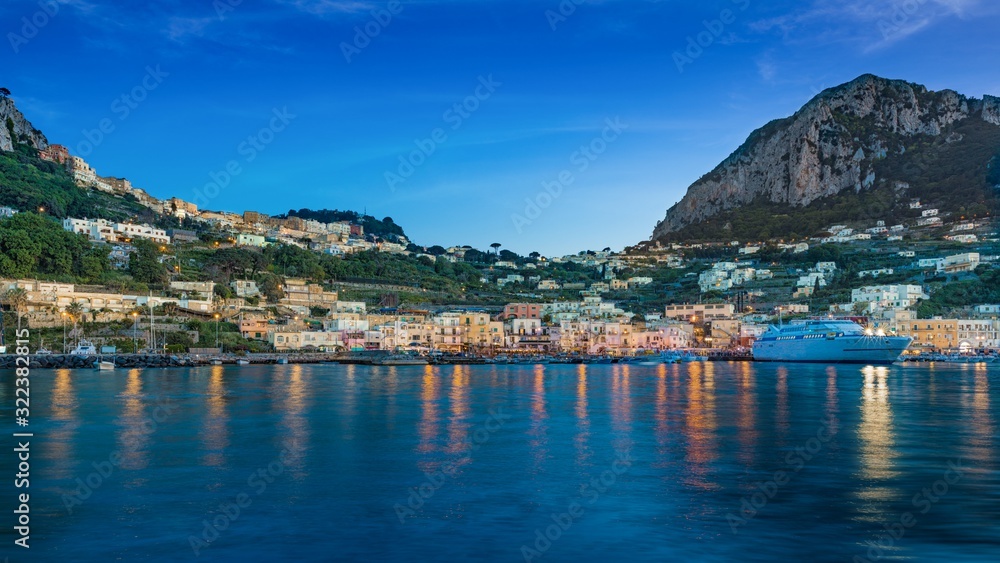 After sunset view of Marina Grande, Capri island, Italy. Illuminated streets of city are reflected in calm sea.