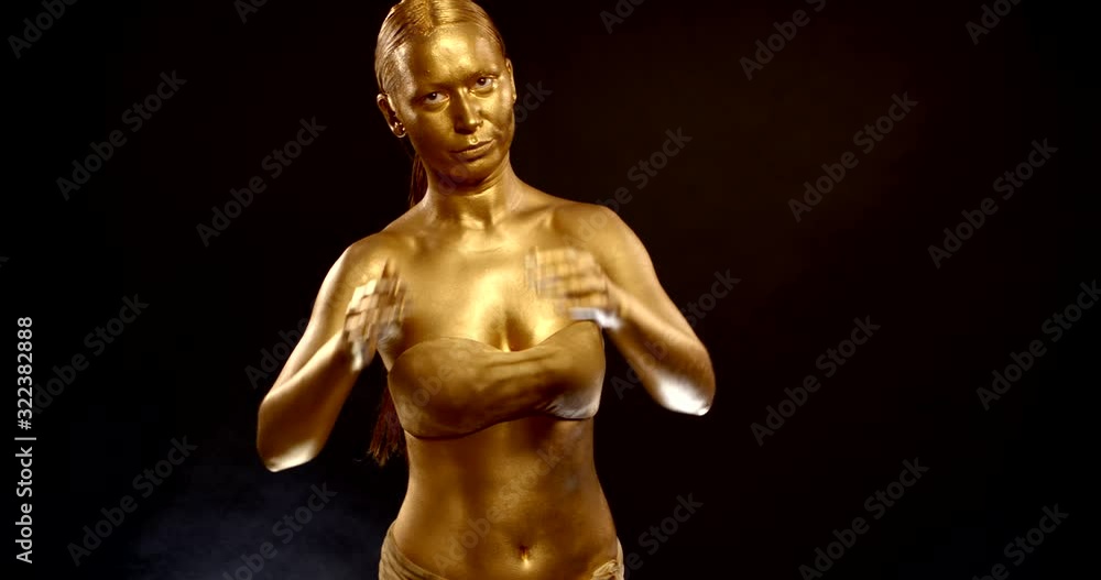 golden goddess is standing and dancing in black background, young woman covered by shiny dye golden goddess is standing and dancing in black background, young woman covered by shiny dye