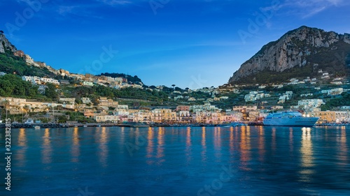 After sunset view of Marina Grande, Capri island, Italy. Illuminated streets of city are reflected in calm sea.