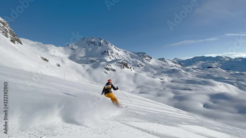 4K skiing footage, one woman skilled skier skiing on ski slope in long turns carving on sunny winter vacation day during ski holidays with clear blue sky high up in european alps mountains splashing s