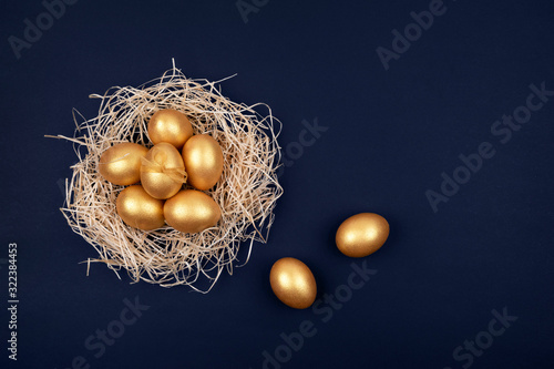 Top view of golden colored Easter eggs in decorative nest on dark blue background. Happy Easter greeting card. Easter background. Place for text.