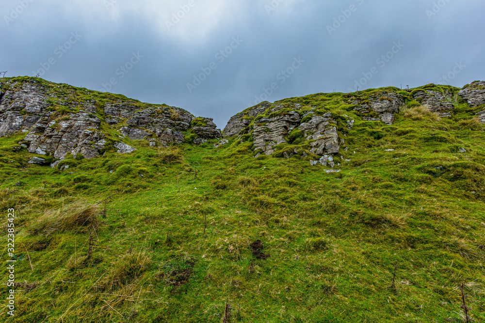 A scenic view of a mountain rock formation with grassy slope under a grey sky