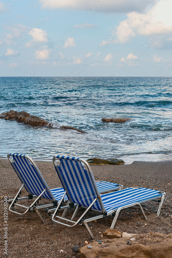sun loungers on a pebble beach of the Greek resort town of Hersonissos on a background of blue sea