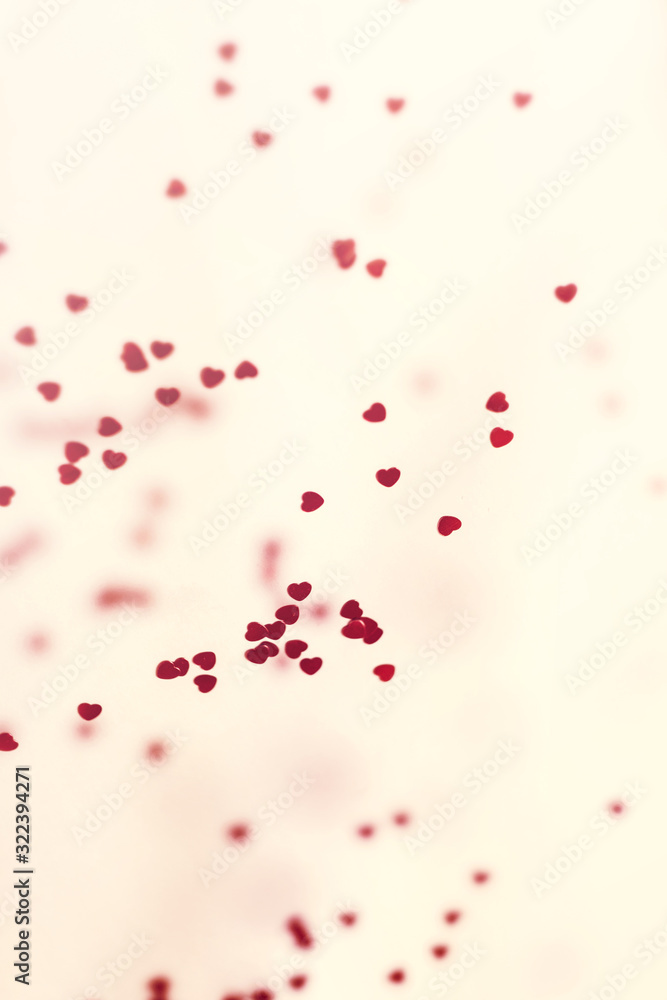 Closeup view of confetti hearts of red color against pink background.