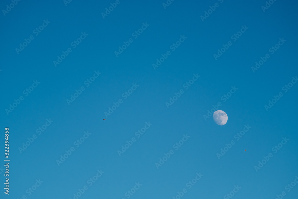 White moon against the blue sky. Full moon in the afternoon. Satellite of the planet earth. Blue skies on a frosty winter day.