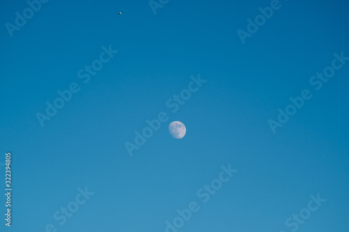 White moon against the blue sky. Full moon in the afternoon. Satellite of the planet earth. Blue skies on a frosty winter day.