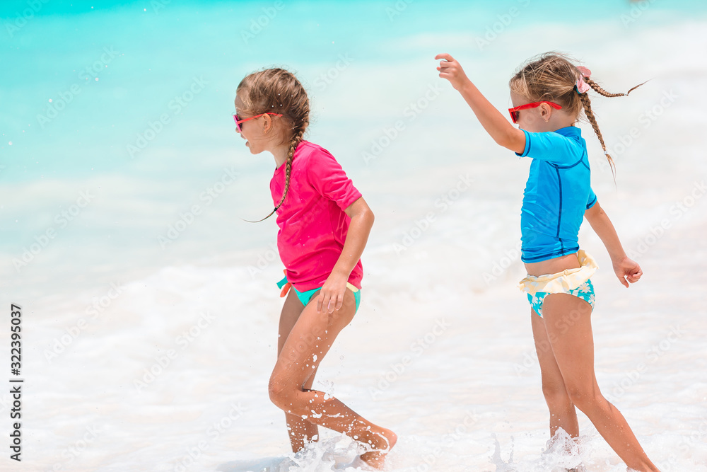 Little happy funny girls have a lot of fun at tropical beach playing together. Sunny day with rain in the sea Little happy funny girls have a lot of fun at tropical beach playing together. Sunny day with rain in the sea
