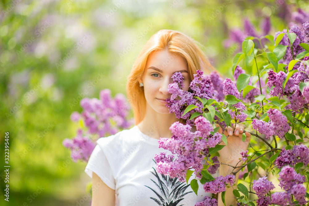 Handsome woman with red hair and pretty smile posing in lilac garden with flowers and enjoys the smell Handsome woman with red hair and pretty smile posing in lilac garden with flowers and enjoys the smell