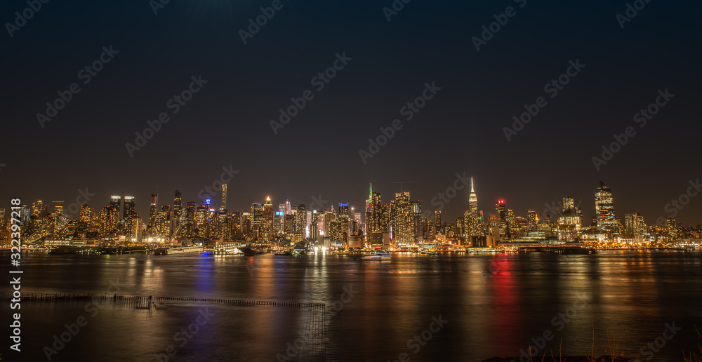 New York City skyline at night with colorful reflections in the Hudson RIver.