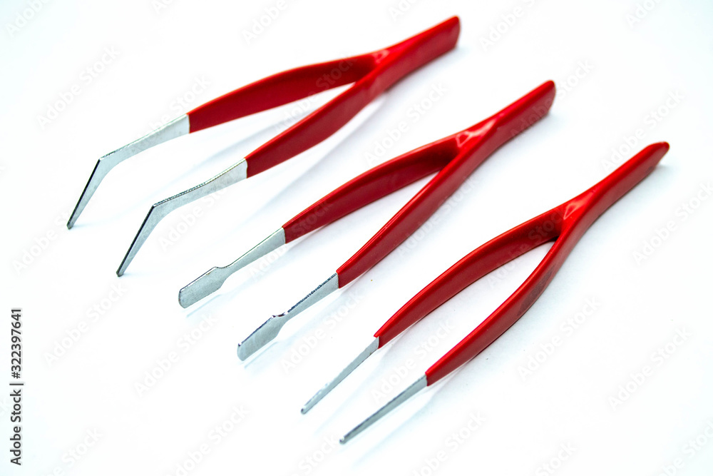 Metal tweezers from technical laboratory isolated on white background. Shot of instruments with a plastic red tools handles to grab things. Metal tweezers from technical laboratory isolated on white background. Shot of instruments with a plastic red tools handles to grab things.
