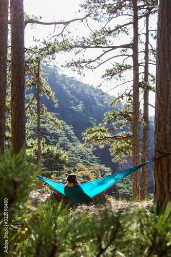 Young woman relaxing in the turquoise hammock in a wood. Concept of relaxation and meditation