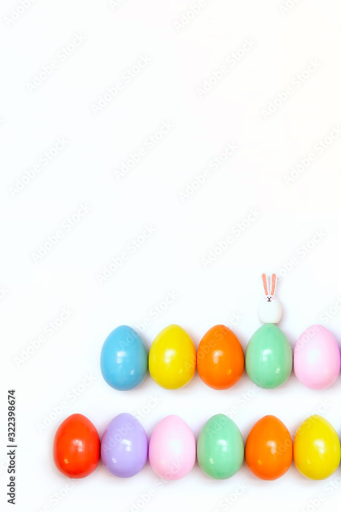 Obraz premium Top view of an Easter composition of painted eggs in bright juicy colors on a white background with a little rabbit. Holiday concept, flat layout, minimalism