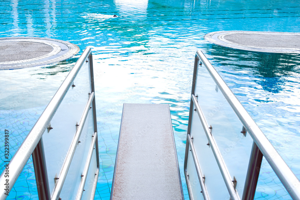Top view close-up on a diving board against the background of a pool with blue water in which a person swims. The concept of summer, relaxation, spa, aqua park, sports, architecture.