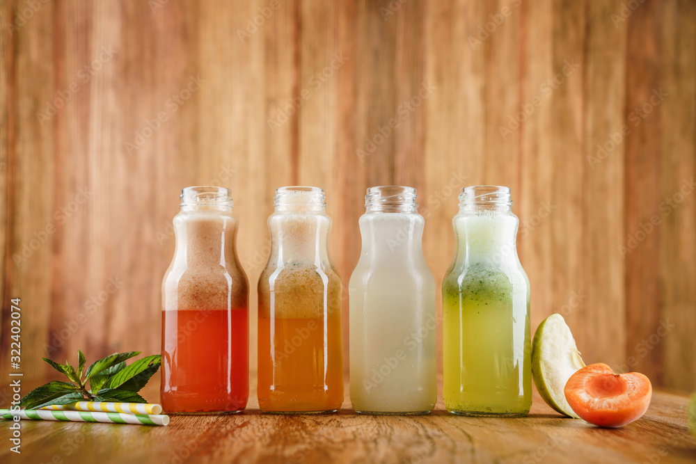 Four lemonade with strawberry, lemon, kiwi, apple, apricot, peach and mint in glass bottles on wooden background. Summer cold drink and beverages Four lemonade with strawberry, lemon, kiwi, apple, apricot, peach and mint in glass bottles on wooden background. Summer cold drink and beverages