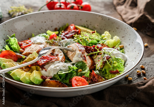 Healthy salad with fillet chicken, avocado, tomatoes, lettuce, greens, pine nuts and sauce in bowl on wooden background. Healthy food, clean eating, dieting, Buddha bowl, close up