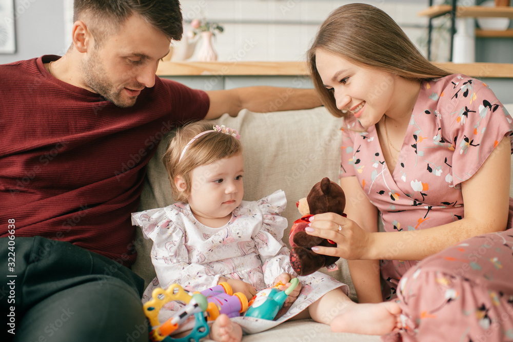 Pretty caucasian mother and strong father in a bright room with his cute little daughter sit on a chair and enjoy the pastime Pretty caucasian mother and strong father in a bright room with his cute little daughter sit on a chair and enjoy the pastime