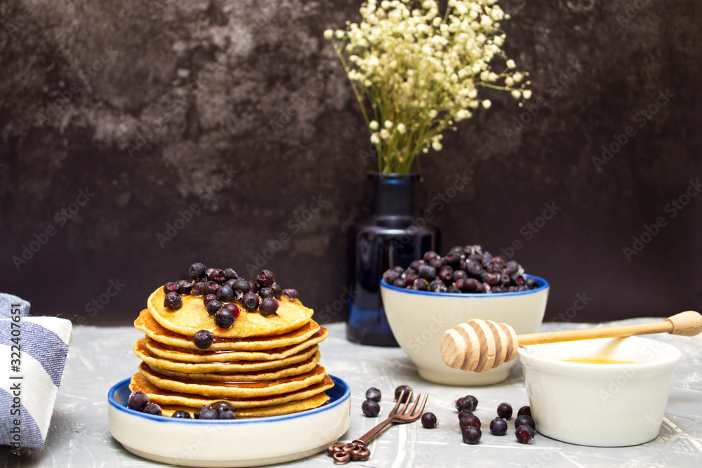 Pancakes with blueberries and honey on a plate. Pancakes and a spoon for honey. Pancakes with blueberries and honey on a plate. Pancakes and a spoon for honey.
