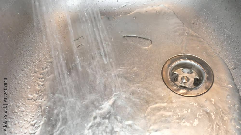 Water spray onto metal drain in stainless steel sink in the kitchen
