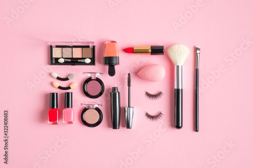 Makeup cosmetic kit. Flat lay composition with lipstick, nail polish, make-up brush, nude eyeshadow palette, false eyelashes on pastel pink background. Makeup artist tools and beauty products set