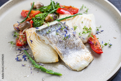 Gourmet fried Italian cod fish filet with broccoli, glasswort and tomatoes as closeup on a modern design plate