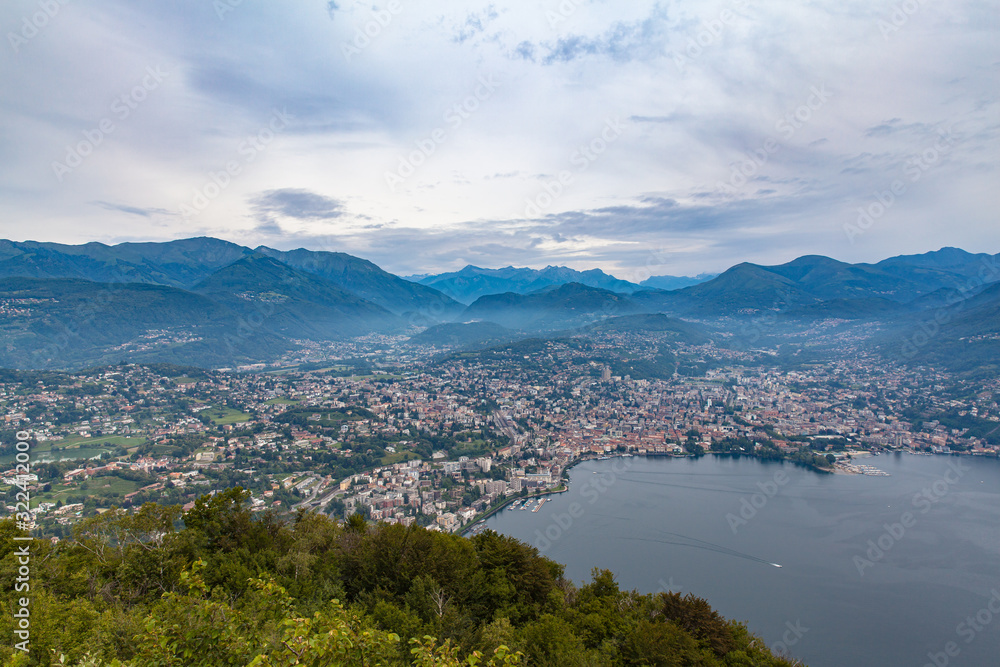 Stunning aerial panorama view of Lugano Lake, cityscape of Lugano, and Swiss Alps mountain on a cloudy summer day from top of Monte San Salvatore, Canton of Ticino, Switzerland