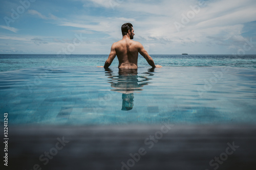 Rear view of man relaxing in infinity pool, Maguhdhuvaa Island, Gaafu Dhaalu Atoll, Maldives photo