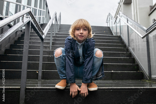 Portrait of blond boy crouching on stairs outdoors photo