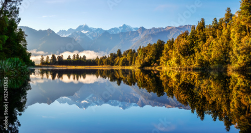 New Zealand, Westland District, Fox Glacier, Lake Matheson reflecting surrounding forest and distant mountain range photo