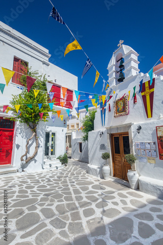 Fototapeta Naklejka Na Ścianę i Meble -  Greek island colorful plaza street with old white architecture buildings and a church in Mykonos, Cyclades, Greece