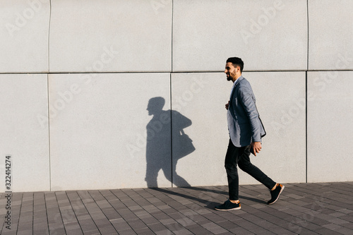 Casual young businessman walking along the wall in the city photo