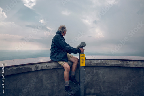 Senior man sitting on wall of observation point, looking at view photo