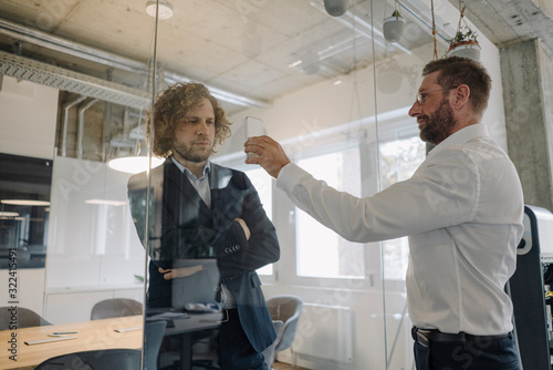 Businessman showing cell phone to colleague behind glass pane