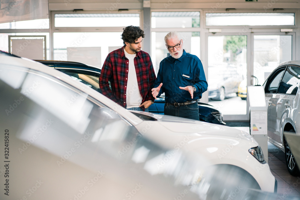 Car dealer showing car to young man in showroom Car dealer showing car to young man in showroom