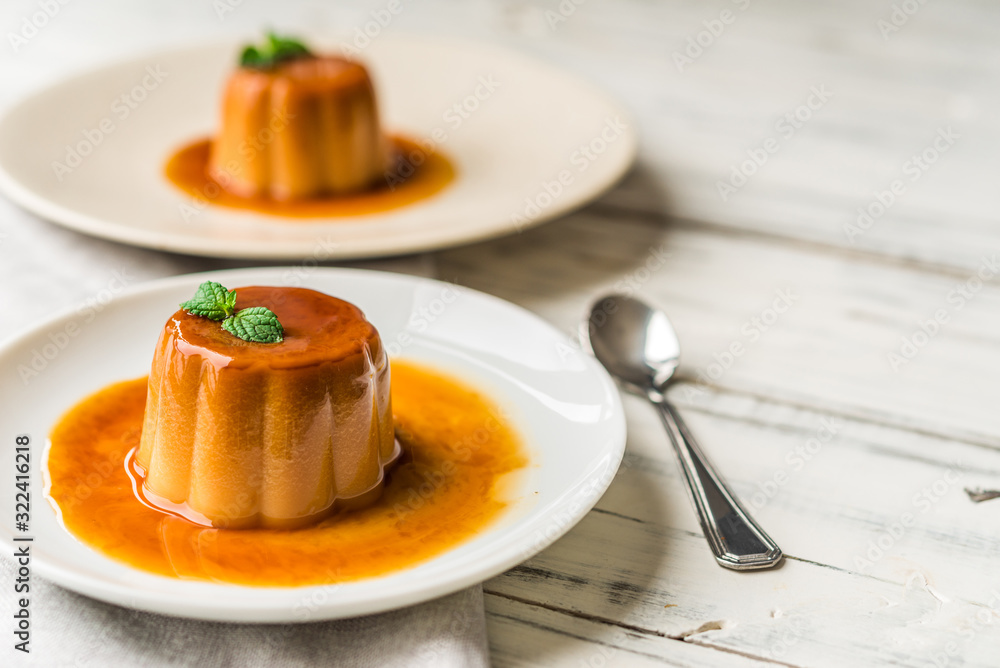 Close up of a flan creme caramel pudding with mint, a custard dessert against white wooden background Close up of a flan creme caramel pudding with mint, a custard dessert against white wooden background