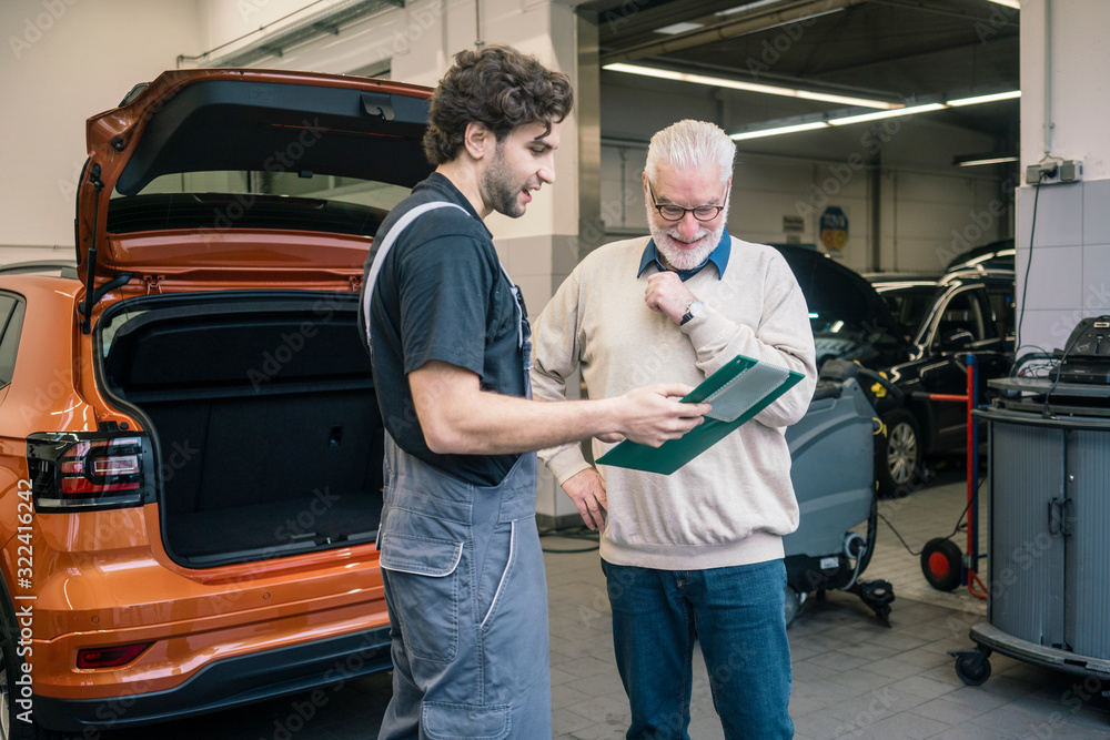 Car mechanic explaining check list to client in workshop Car mechanic explaining check list to client in workshop