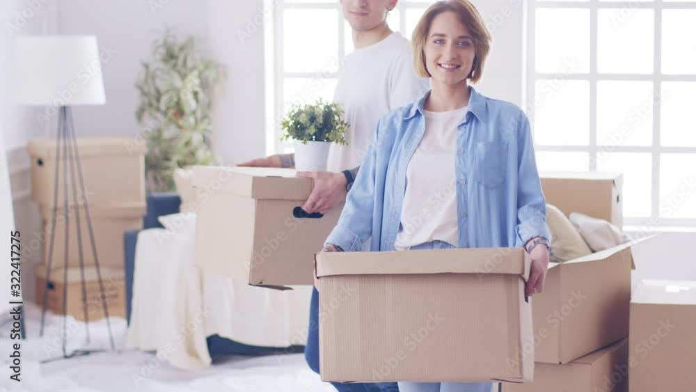 Happy couple first time home buyers holding boxes talking embracing standing in hallway. Happy couple first time home buyers holding boxes talking embracing standing in hallway.