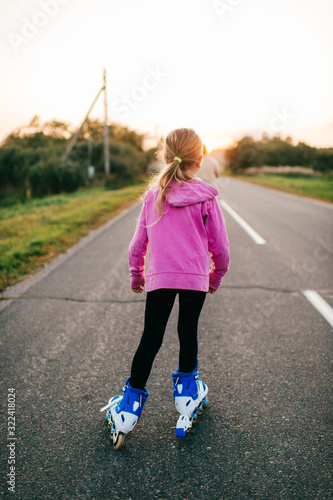 Pretty young girl in pink hoody roller-skates on the village road in the evening © benevolente
