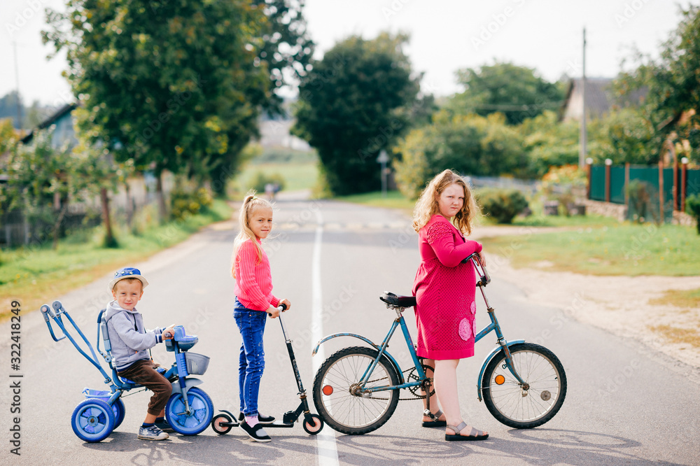 Brothers and sisters stands on the village road together with bicycles Brothers and sisters stands on the village road together with bicycles
