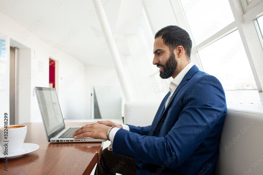 young successful businessman use a laptop and drink coffee in the morning at work, a freelancer is sitting with a computer in a white cafe young successful businessman use a laptop and drink coffee in the morning at work, a freelancer is sitting with a computer in a white cafe